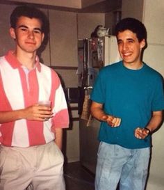 two young men standing next to each other in front of a refrigerator with magnets on it