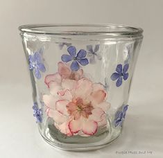 a glass vase with pink and blue flowers painted on the inside, sitting on a white surface