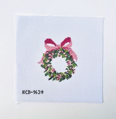 a cross - stitch christmas card with a pink bow and a wreath on the front