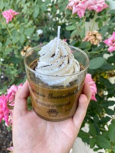 someone is holding up a cup of coffee with whipped cream on top and flowers in the background