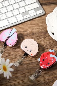 three keychains with cartoon characters on them sitting next to a keyboard and flower