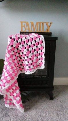 a pink and white crocheted blanket sitting on top of a black dresser next to a sign that says family