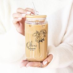 a woman holding a mason jar filled with liquid and flowers on the inside, while wearing a white sweater