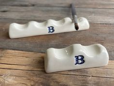 two ceramic toothbrush holders with the letters b and person on them sitting on a wooden table