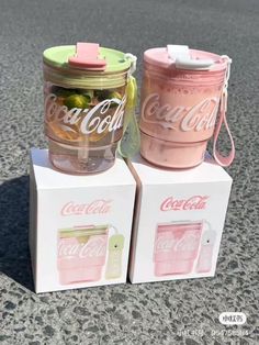 two pink and green coca - cola cans sitting on top of each other in front of a white box