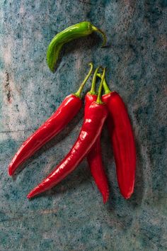 three red chili peppers on a blue surface with one green pepper in the foreground