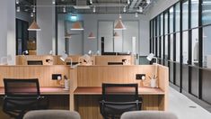 an empty office with desks and chairs in the foreground, lights above them