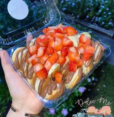 a person holding up a tray of food with strawberries on it and chocolate sauce