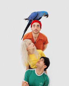 three people sitting on top of each other with a parrot perched on their shoulders over them