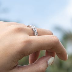 a woman's hand holding an engagement ring in front of the camera with trees in the background