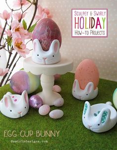 an egg cup bunny is surrounded by other easter decorations and eggs on green grass with pink flowers in the background