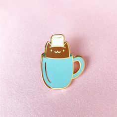 a cat in a cup pin sitting on top of a pink surface