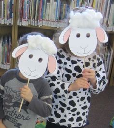 two children with paper sheep masks in front of bookshelves at the school library