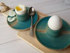 two plates with spoons and an egg on them sitting on a wooden tray next to each other