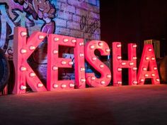 the word keesha is lit up in front of a brick wall