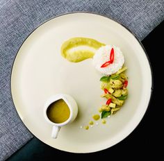 a white plate topped with food next to a cup of green liquid and sauce on top of it