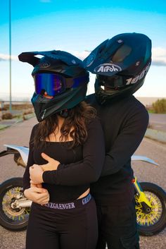 two people standing next to each other in front of a motorcycle with helmets on their heads