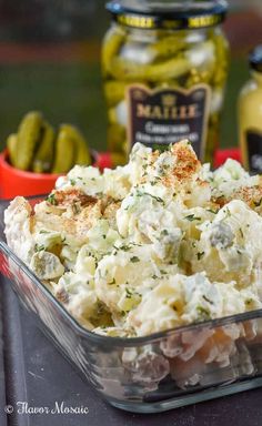 a glass dish filled with potato salad next to pickles