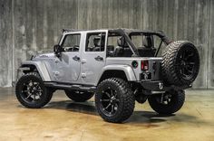 a silver jeep parked in front of a concrete wall with black tires and rims