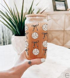 a person holding up a drink in front of a table with a potted plant