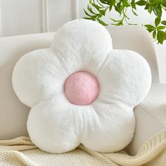 a flower shaped pillow sitting on top of a white couch next to a potted plant