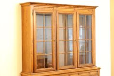 a wooden china cabinet with glass doors on the top and bottom, against a yellow wall