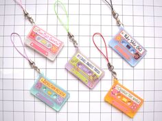 four cassette shaped keychains are hanging on a white gridded surface, one has a tape recorder and the other has an mp3 player attached to it