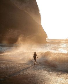 a person is running on the beach in front of an ocean cliff and water spray