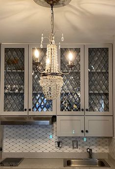 a chandelier hanging from the ceiling in a kitchen with white cabinets and counter tops