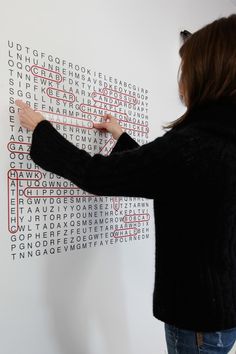 a woman writing on a white wall with red and black letters in the form of words