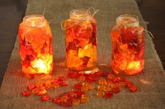 three jars filled with orange and red leaves on top of a burlap table