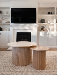 a living room with two round tables and a television on the wall above it in front of a fireplace