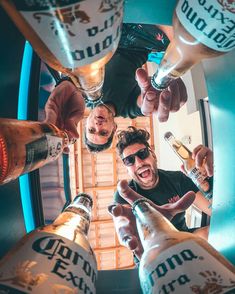 three men are standing in a circle holding beer bottles and pointing at the camera with their thumbs up