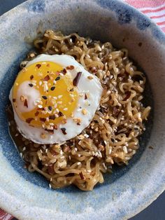 a bowl with noodles, an egg and sesame seeds in it on a striped table cloth