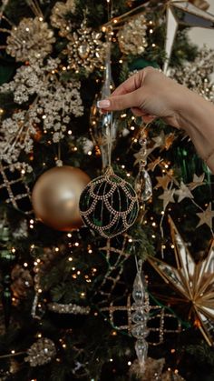 a person holding an ornament in front of a christmas tree with gold and silver decorations