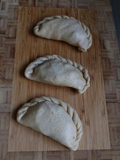 three uncooked pastries sitting on top of a cutting board next to each other