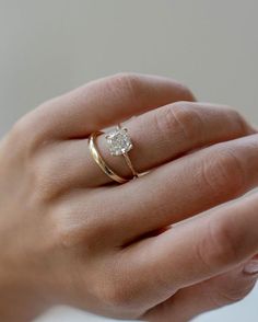 a woman's hand wearing a gold ring with a white diamond in the middle