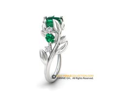 a white gold ring with green stones and leaves on the side, set in 18k white gold