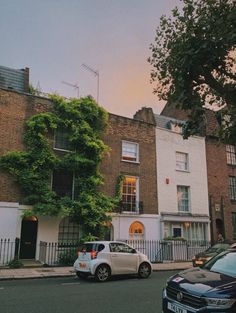 two cars are parked on the street in front of some brick buildings with ivy growing over them