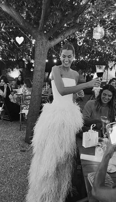 a woman in a white dress standing next to a tree with people sitting around it