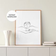 a poster with a hand holding a baby's foot on it next to a white vase