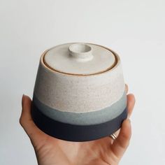 a hand holding a white and blue ceramic container with a black band around the top