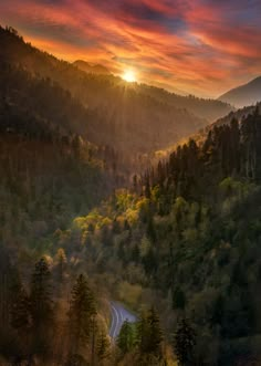 the sun is setting over a mountain valley with trees and hills in the foreground