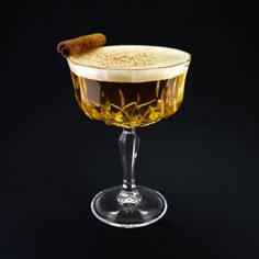 an alcoholic drink in a glass with a cinnamon stick sticking out of the top, on a black background