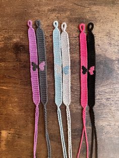 three crocheted lanyards are shown on a wooden surface, one is pink and the other is gray