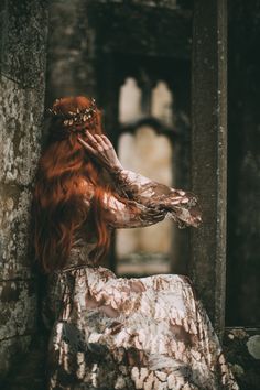 a woman with red hair is sitting in an old building wearing a dress and crown