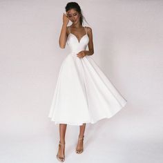 a woman in a white dress posing for the camera with her hand on her head