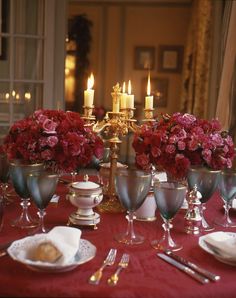 the table is set with silverware and red flowers