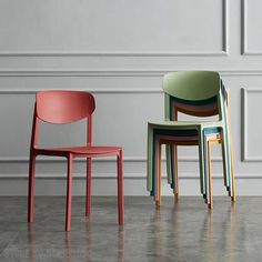 three different colored chairs sitting next to each other on the floor in front of a white wall