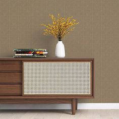 a white vase with yellow flowers sitting on top of a wooden dresser next to a brown wall